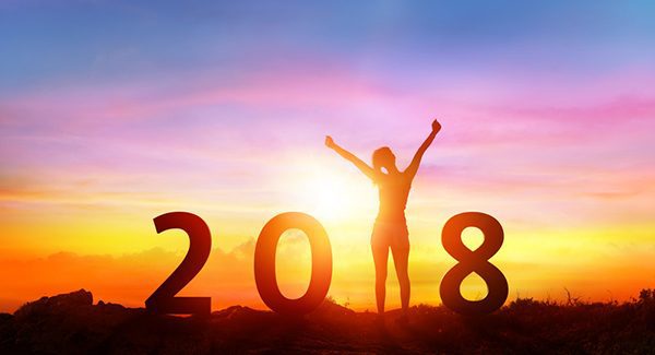 A motivated woman standing in front of a yellow, purple and pink sunset with her arms in the air. She is the 1 in a sign that says 2018